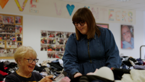 Photo shows Volunteer Manager Lindsay showing a volunteer how to label the products