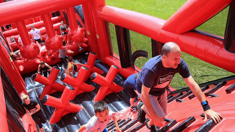 Image shows a man climbing on a large red inflatable as part of a challenge event to fundraise for Newlife