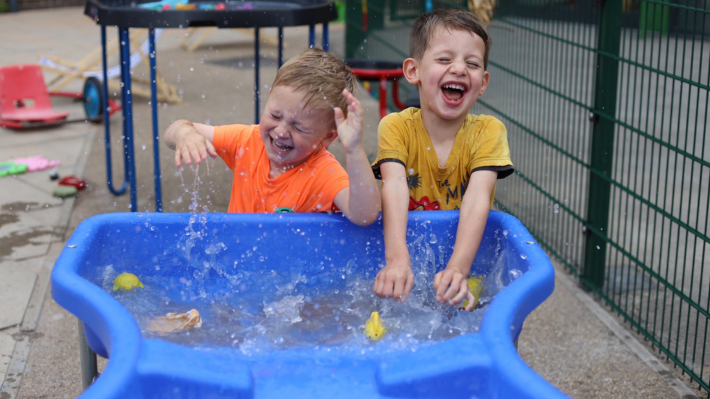 Picture shows two young children splashing on a wet play table at a childcare setting with Newlife charity