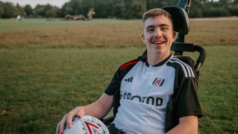 Image shows young teenager in an adapted wheelchair with a football