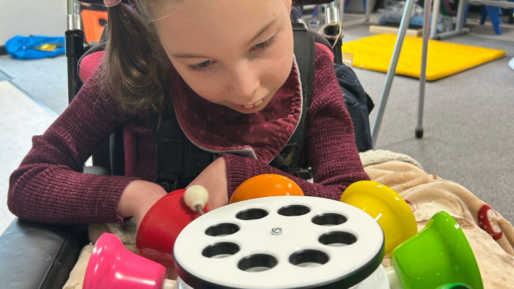 The image shows a child playing with a sensory toy in a childcare setting.