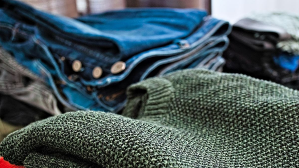 Image shows jumpers and jeans piled up on a table
