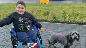 Image shows a boy in a wheelchair with his dog on a lead